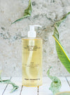 Botanical Protein Complex Shampoo with gold liquid on white tile surface and marble background. Leaves around the bottle.