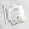 Two Intense Recovery Treatment Masks in silver pouches stacked on a gray and white marble counter background..